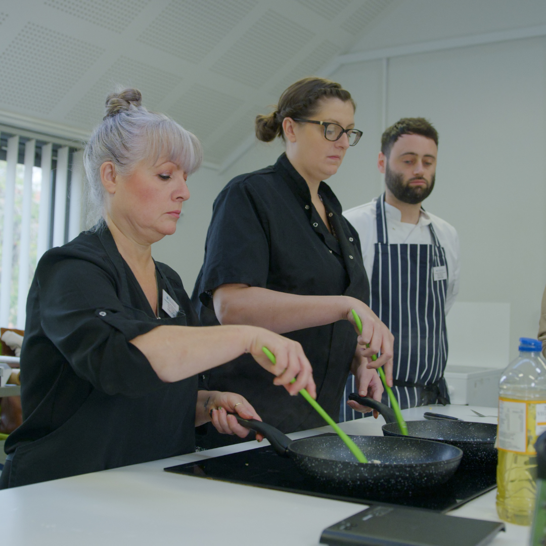 two women cooking, a man in the background